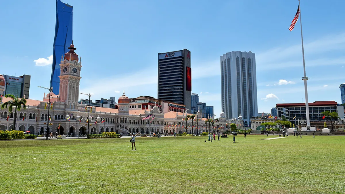 Dataran Merdeka (Independence Square) A large grassy field in front of historic colonial buildings and modern skyscrapers, with a tall flagpole and Malaysian flag