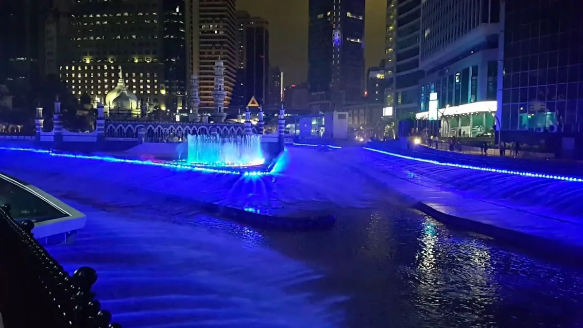 Kolam Biru, or the Blue Pool Nighttime city fountain lit in blue between tall buildings