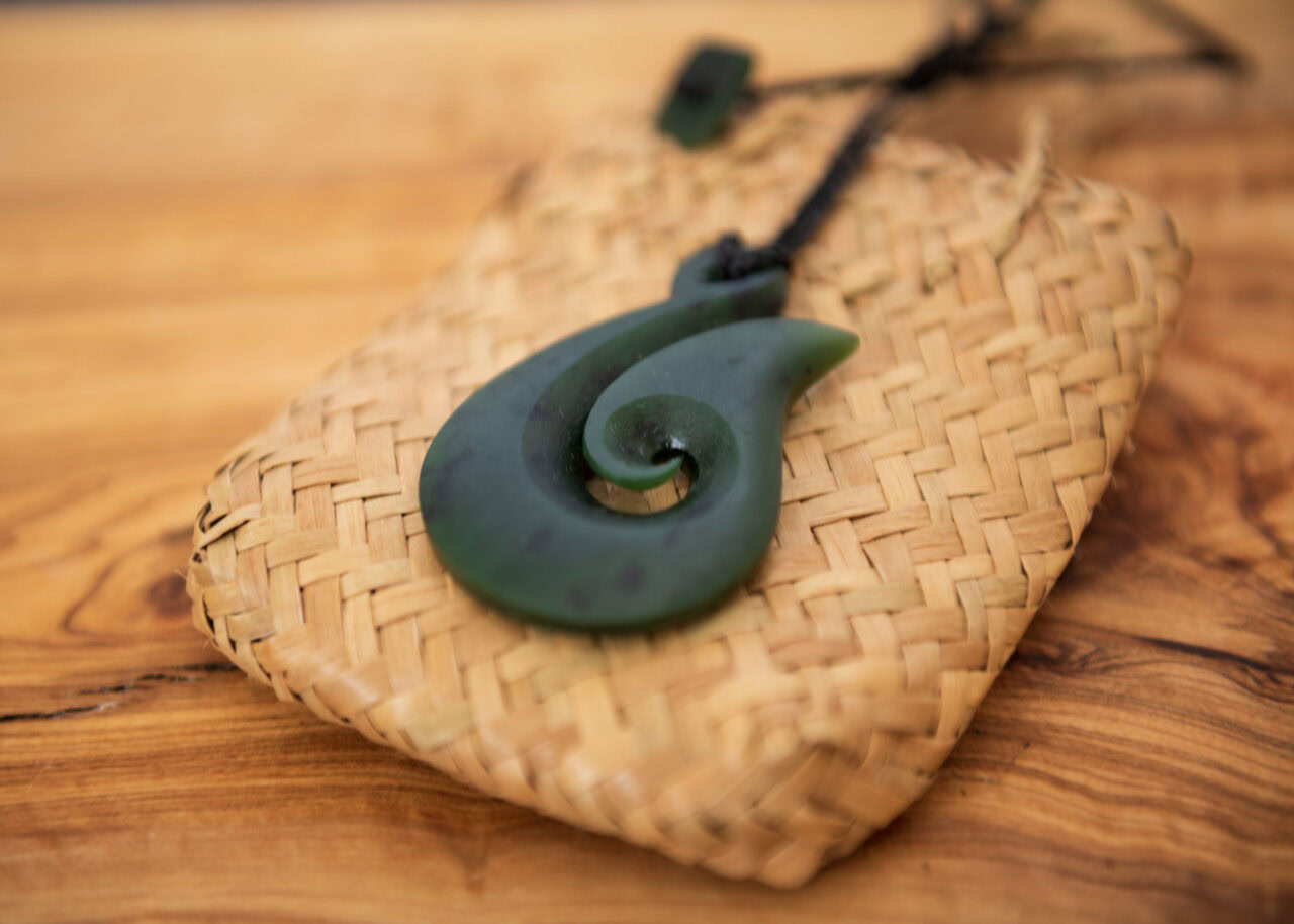 pounamou-1280x914-1 Pounamu fish hook necklace on wooden background.